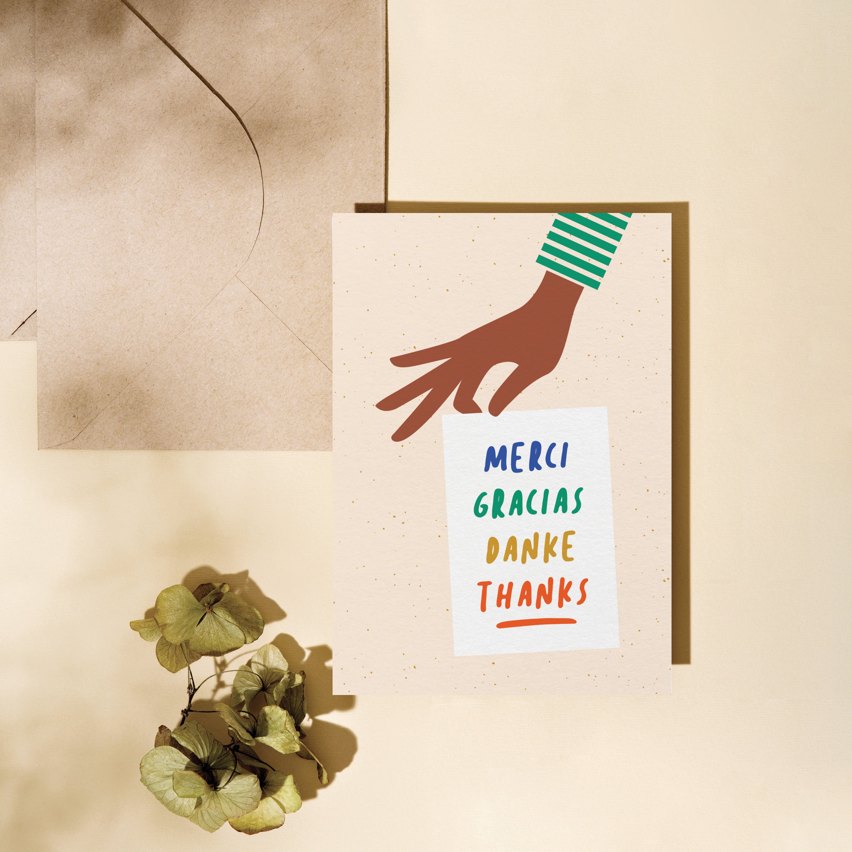 thank you card with a hand holding a white paper with a text in it that says Merci, Gracias, Danke Edit alt text