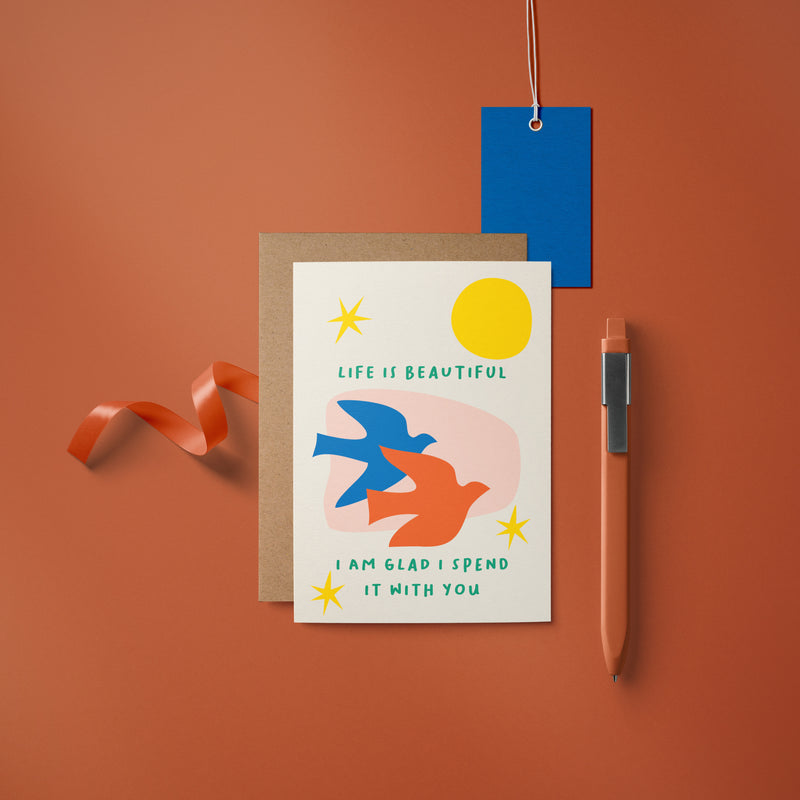 Love card with blue and red birds, yellow sun, yellow stars and a text that says Life is beautiful i am glad i spend it with you  Edit alt text