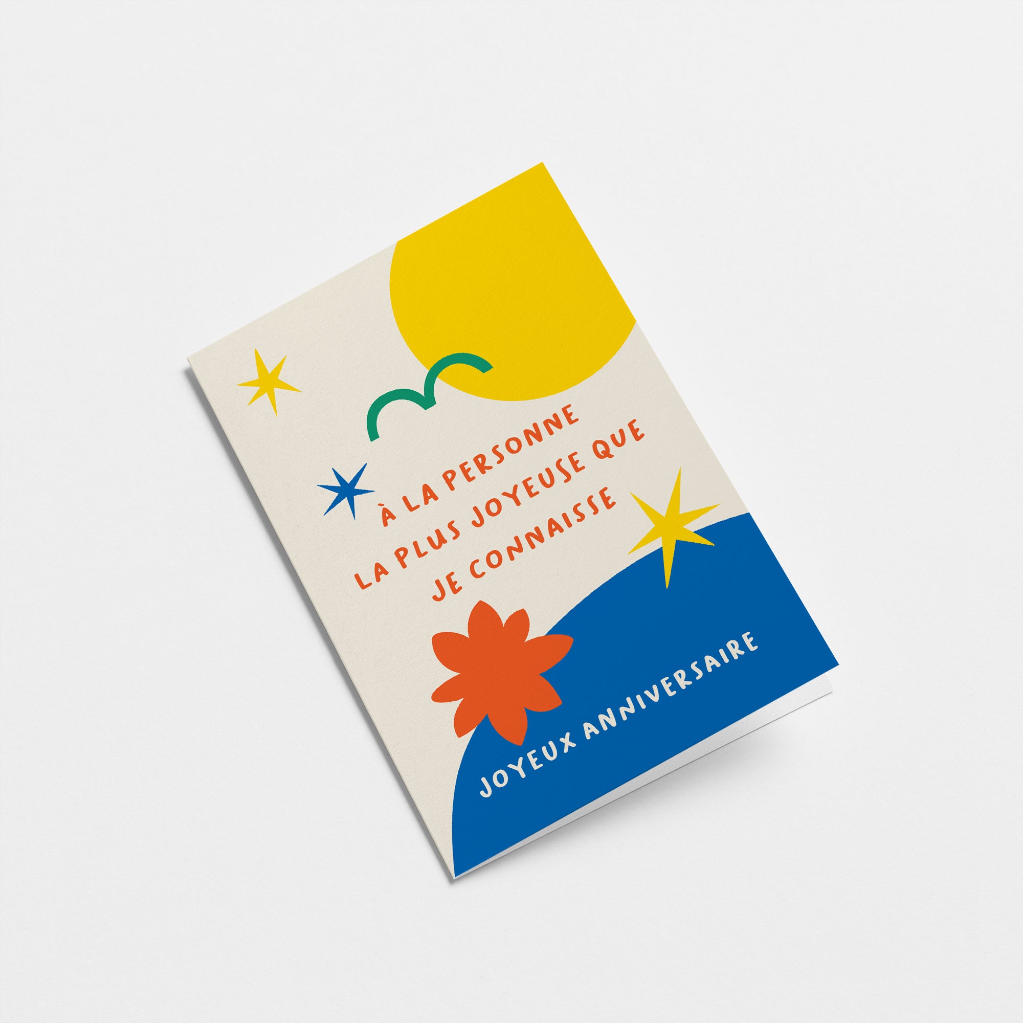 French birthday card with yellow sun green bird yellow stars blue figures and a text that says À la personne la plus joyeuse que je connaisse, joyeux anniversaire  Edit alt text