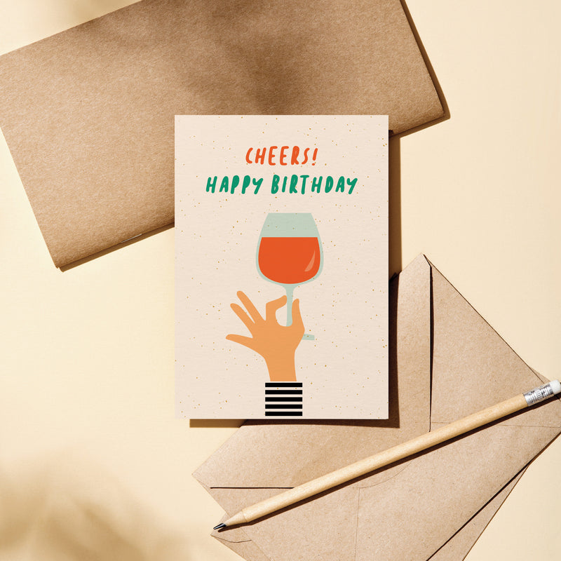 Birthday card with a hand holding a glass of wine and a text that says Cheers! Happy Birthday  Edit alt text