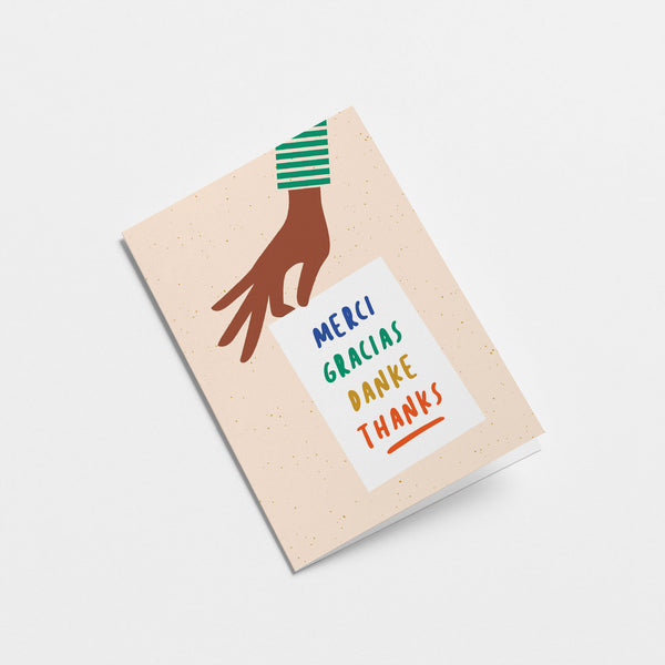 thank you card with a hand holding a white paper with a text in it that says Merci, Gracias, Danke  Edit alt text