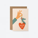 christmas card with a hand holding red christmas tree ornament and a text in it that says christmas love  Edit alt text