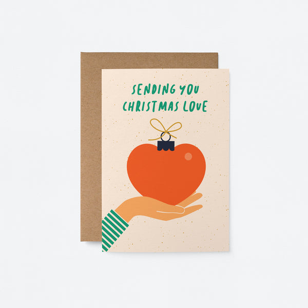 Christmas card with a hand holding a red heart with a gift ribbon on top of it and a text that says sending you christmas love
