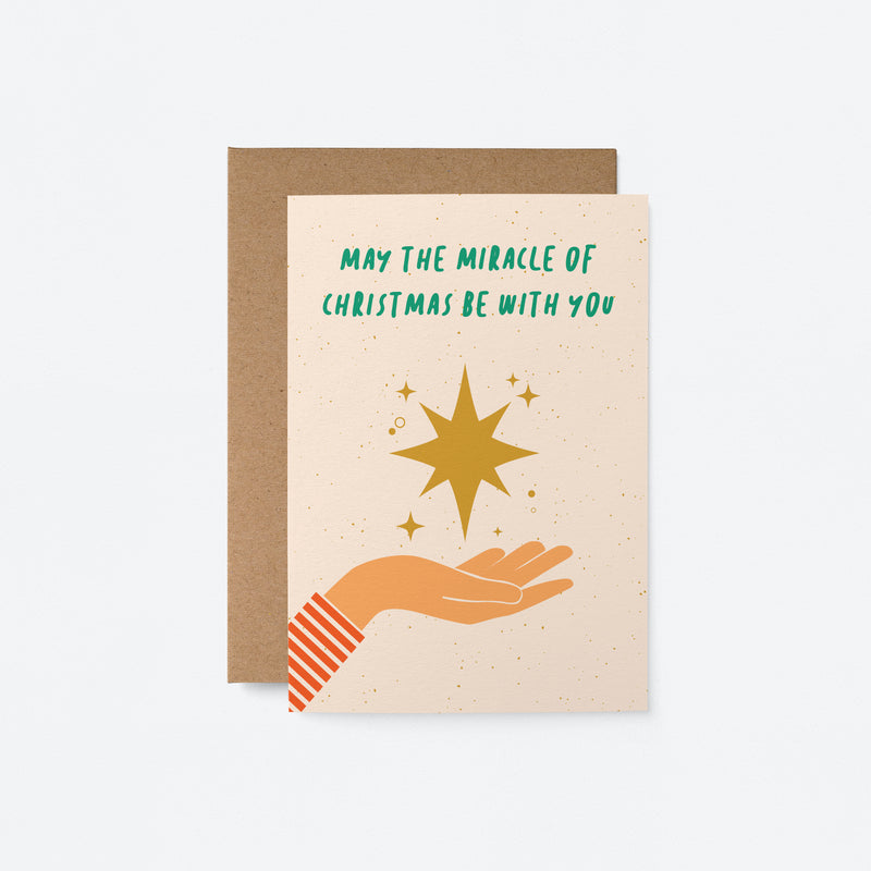 Christmas card with a yellow christmas ornament star on the palm of a hand with a text that says may the miracle of christmas be with you