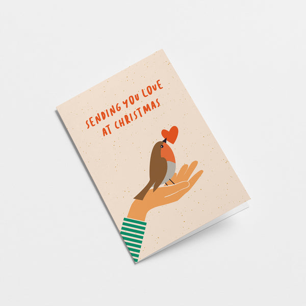 Christmas card with a bird and a red heart in its beak on the palm of a hand and a text that says sending you love at christmas  Edit alt text