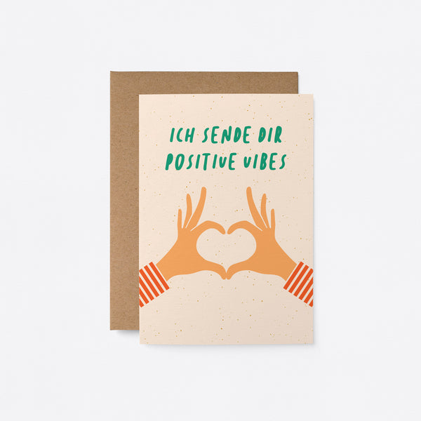 German greeting card with two hands creating heart shape with fingers and a text that says Ich sende dir positive Vibes