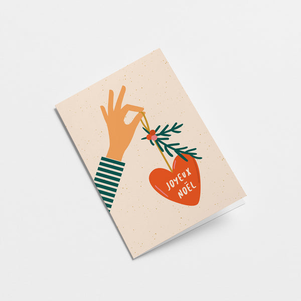 french christmas card with a hand holding red christmas tree ornament and a text in it that says Joyeux Noël  Edit alt text