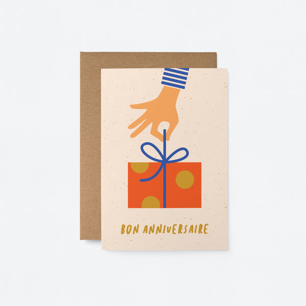 french birthday card with a hand holding a blue ribbon of a red birthday present and a text that says Bon anniversaire